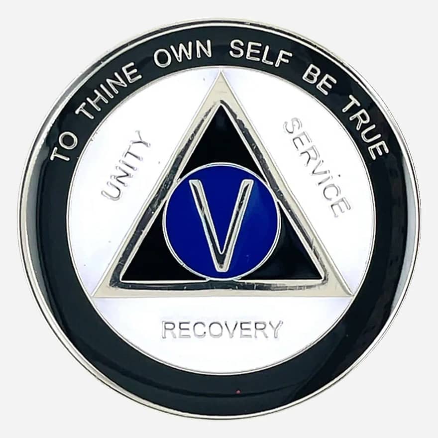 A distinctive AA sobriety medallion (approximately 34mm) featuring a bold black outer enamel ring and a crisp white inner ring. The center prominently displays a blue AA circle and triangle symbol, surrounded by the words 'Unity,' 'Service,' and 'Recovery.' The outer edge includes 'To Thine Own Self Be True' and the sobriety anniversary year (in Roman numerals, 1-40 years). The token has a smooth, glossy finish that highlights its contrasting colors.