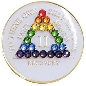 A white coin with rainbow colored stones in the shape of a triangle.