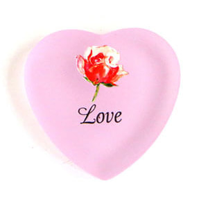 A pink heart shaped plate with the word love and a rose on it.