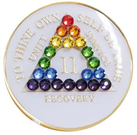 A white coin with rainbow colored stones in the shape of a triangle.