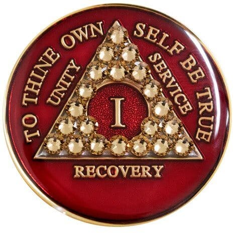 A red and gold sobriety chip with the letter i.