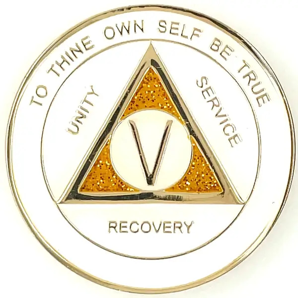 A white and gold sobriety coin with the words recovery written on it.