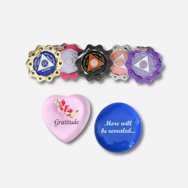 A collection of unique recovery gifts featuring a Bike Chain Medallion Holder, a Language of Flowers Heart with a Sweet Pea representing "Gratitude", and a More Will Be Revealed Stone in Blue/White.